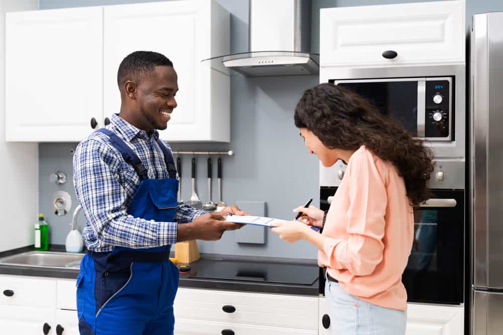 Smiling Customer Woman Signing Appliance Repair Invoice In Front Of Employee
