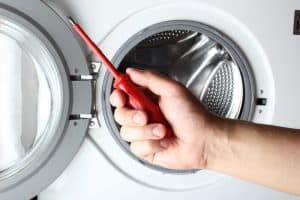 Technician holding red screwdriver in front of washing machine